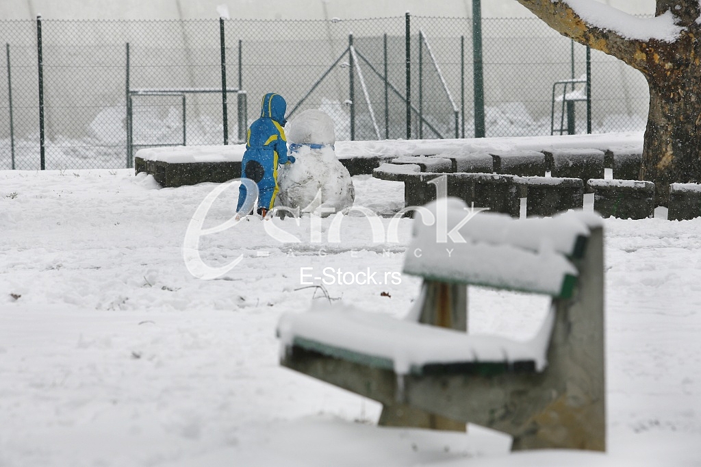 Joyful boy sculpts a snowman in park