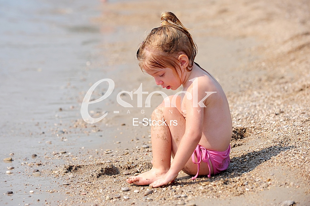 little girl sitting on the beach and playing in the sand